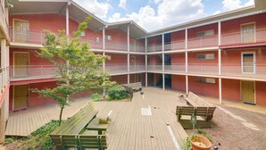 A multi-story building with a courtyard featuring wooden benches and a small tree. - 1 Mi to Dtwn & Uga: Condo w/ Pool in Athens! (Athens)