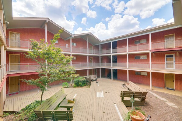A multi-story building with a courtyard featuring wooden benches and a small tree. - 1 Mi to Dtwn & Uga: Condo w/ Pool in Athens! (Athens)