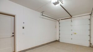 Eine saubere, leere Garage mit einer weißen Tür, einem Metalllüfter und einem Betonboden.