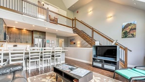 A spacious living area with a high ceiling, a staircase, a kitchen with wooden cabinets, a dining area with white chairs, and a flat-screen TV. - Ski-in/ski-out Gemini Lift Access! Home w/ Hot Tub (Winter Park)