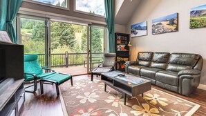 A spacious living room with a large window, a green chair, a leather sofa, a coffee table, and a bookshelf. - Ski-in/ski-out Gemini Lift Access! Home w/ Hot Tub (Winter Park)