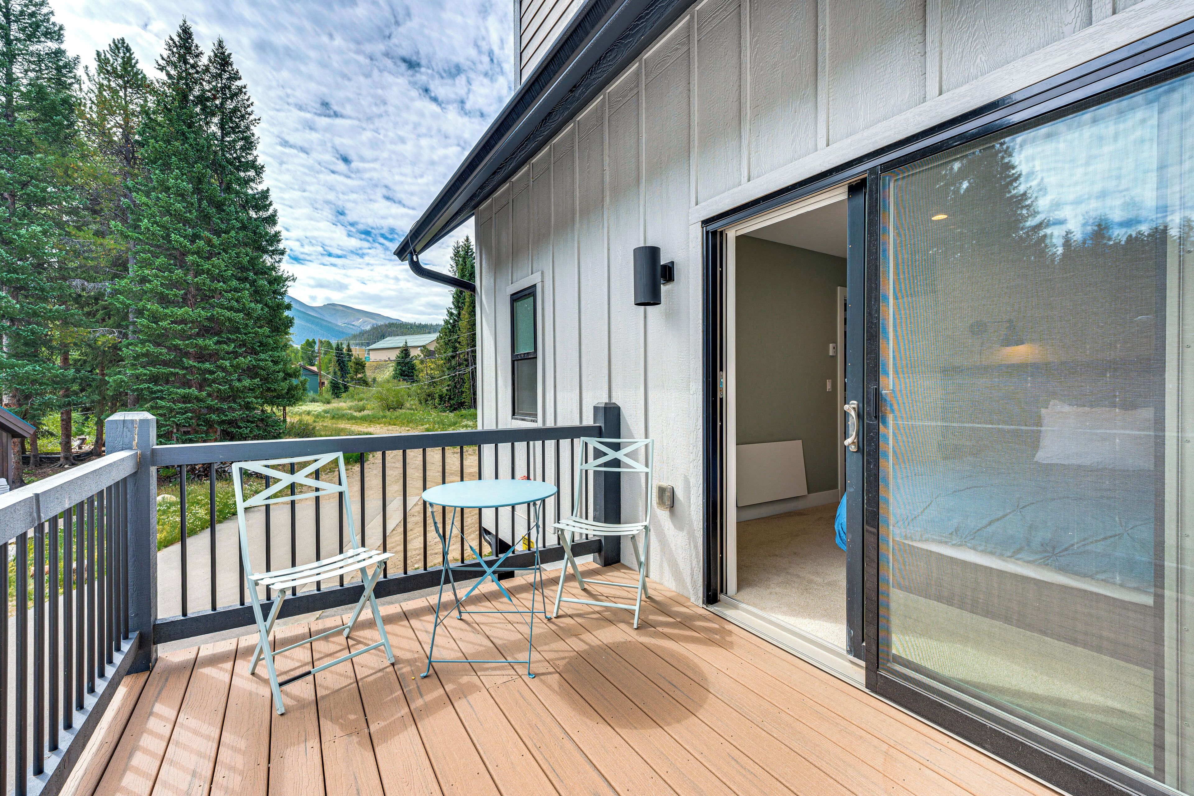 A wooden deck with a table and chairs, a glass door, and a view of trees and mountains.