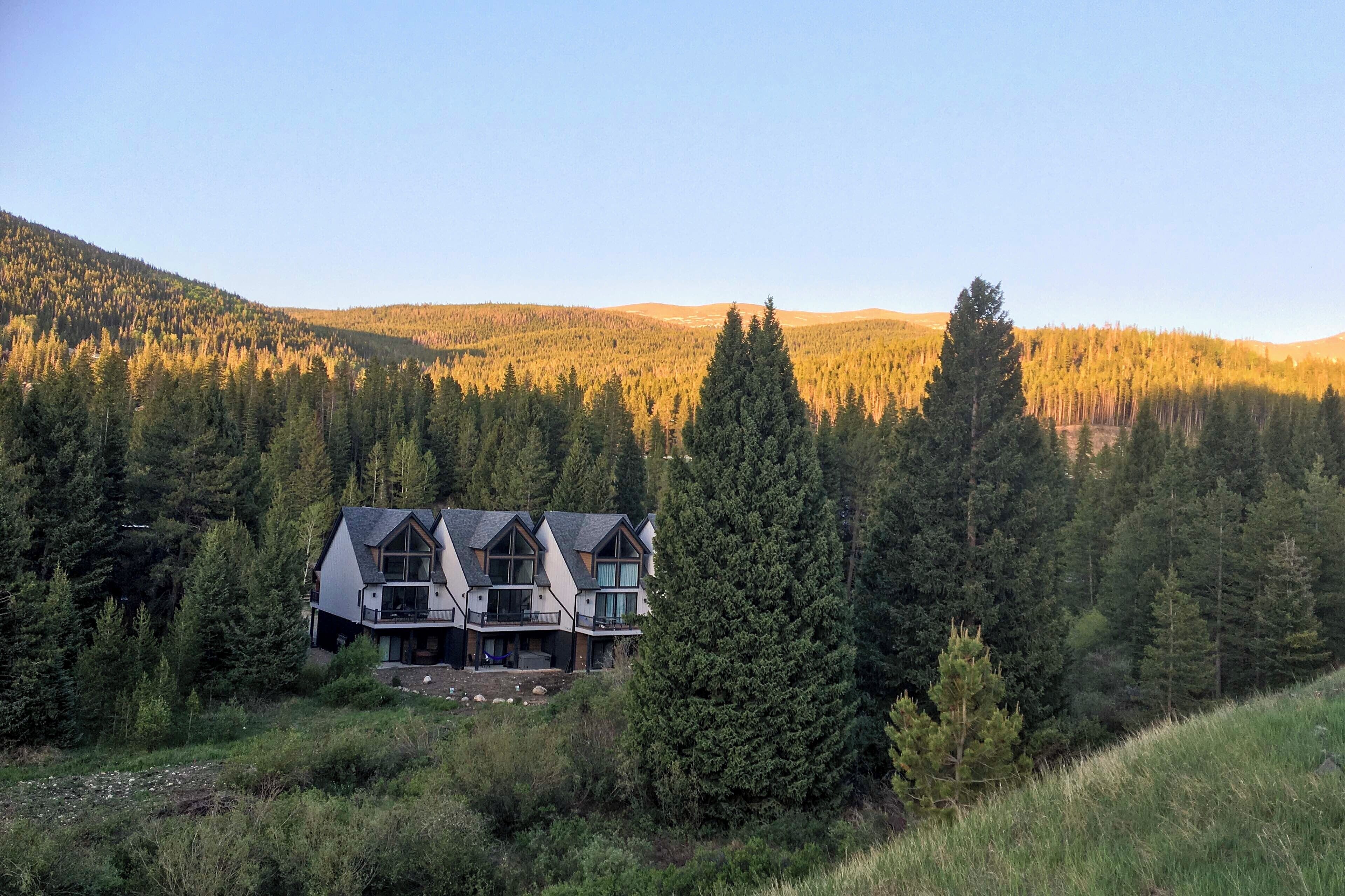 Una casa grande de varios pisos rodeada de un bosque denso, con una montaña destacada al fondo.