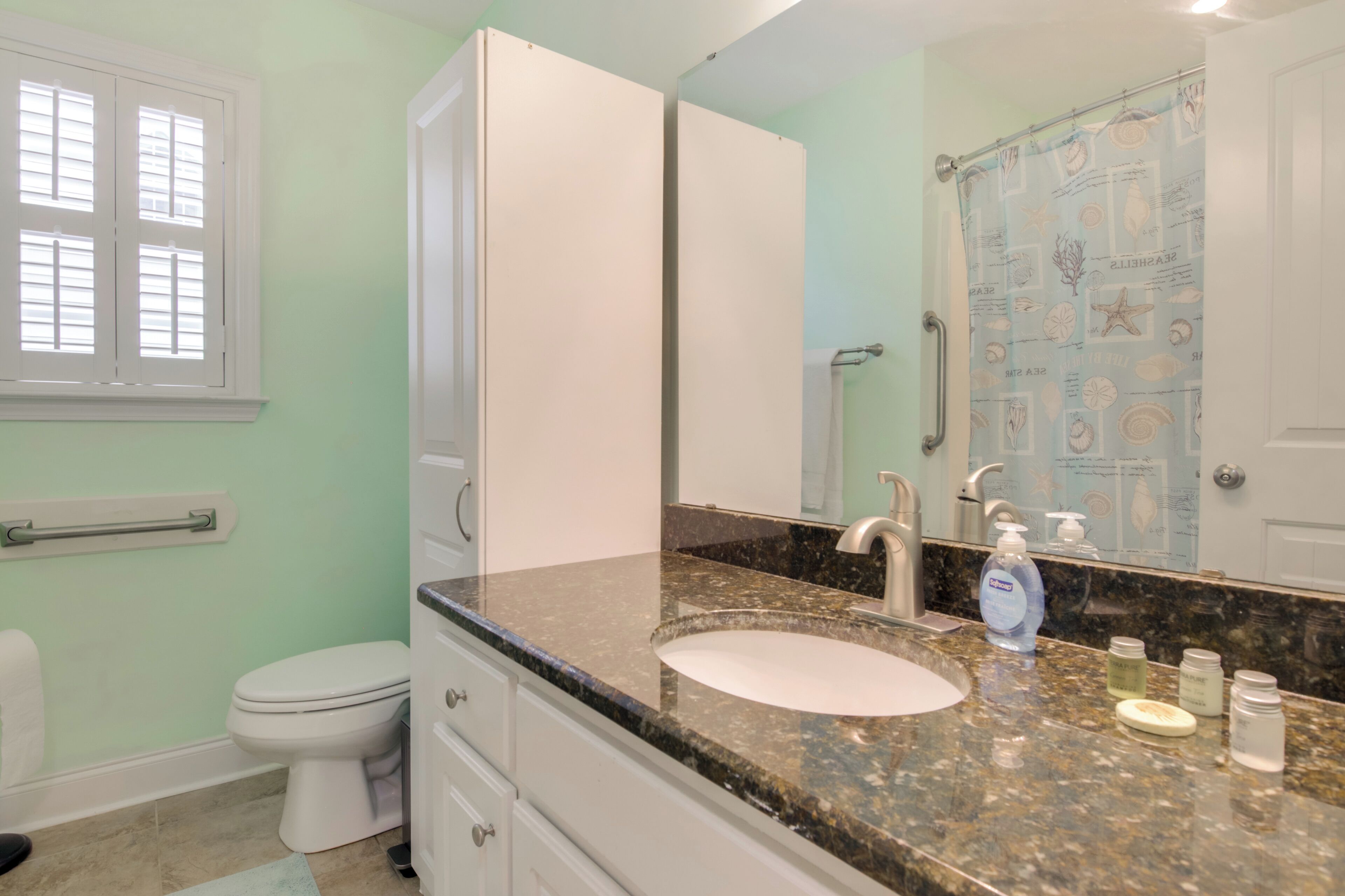 A bathroom with a white toilet, a sink with a granite countertop, a mirror, and a shower curtain with a nautical theme.