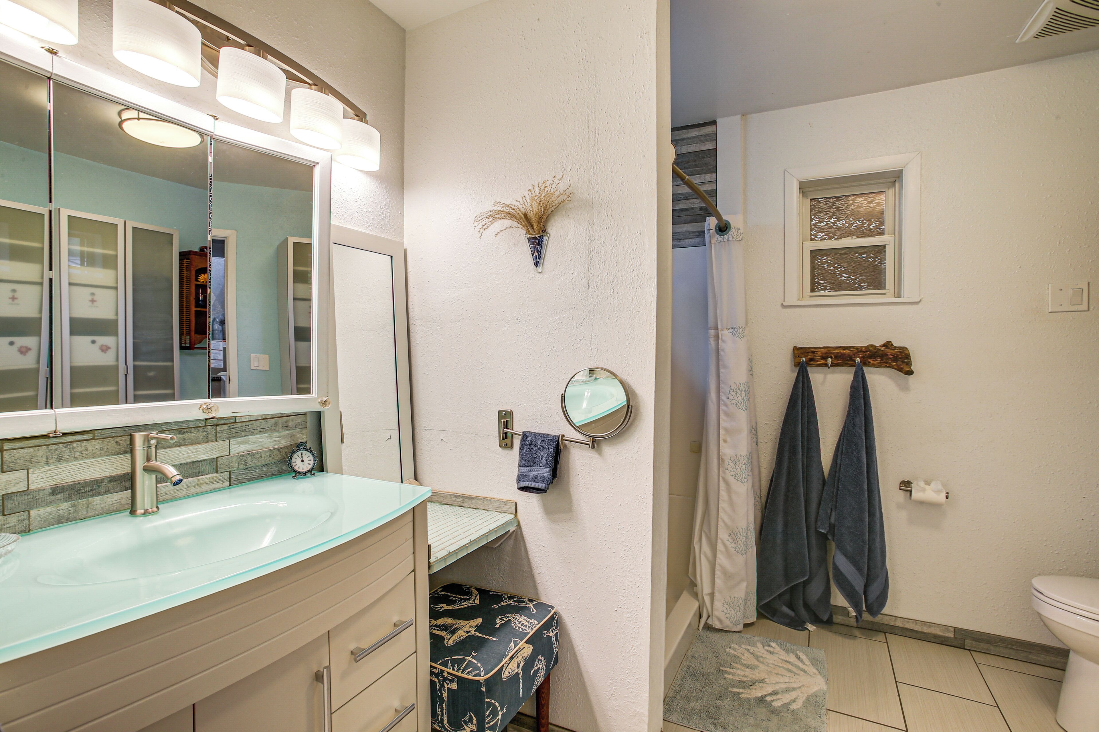 A bathroom with a glass sink, a mirror, a towel rack, and a shower curtain.