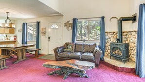 A cozy living room with a stone fireplace, a leather sofa, a wooden coffee table, and a dining table with chairs. - Hike, Swim, Golf: Family Retreat in Arnold! (Arnold)
