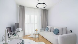 A modern living room with a white sofa, a dining table with a white candle, and a glass coffee table. - Modern Studio in the Center of Poznań | Smart TV (Poznań)