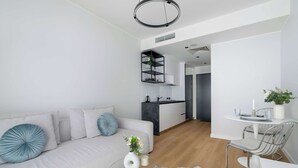 A modern living room with a sofa, a glass coffee table, and a dining area with a chair and table. - Modern Studio in the Center of Poznań | Smart TV (Poznań)