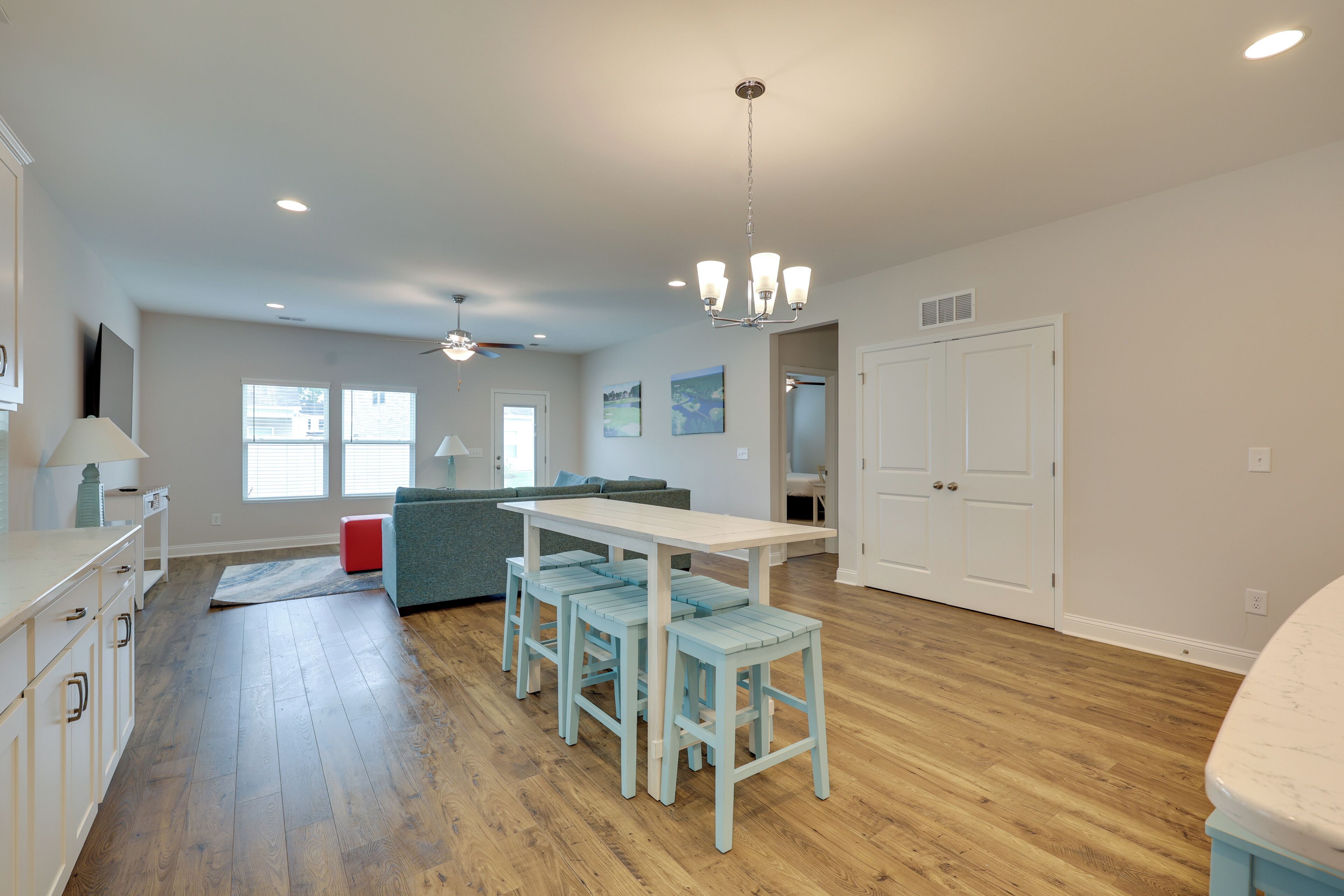 A spacious kitchen with a wooden floor, a white dining table with blue chairs, and a ceiling fan.