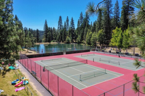 An outdoor tennis court surrounded by trees and a lake. - Walk to Fly-in Lake: Blue Lake Springs Cabin! (Arnold)