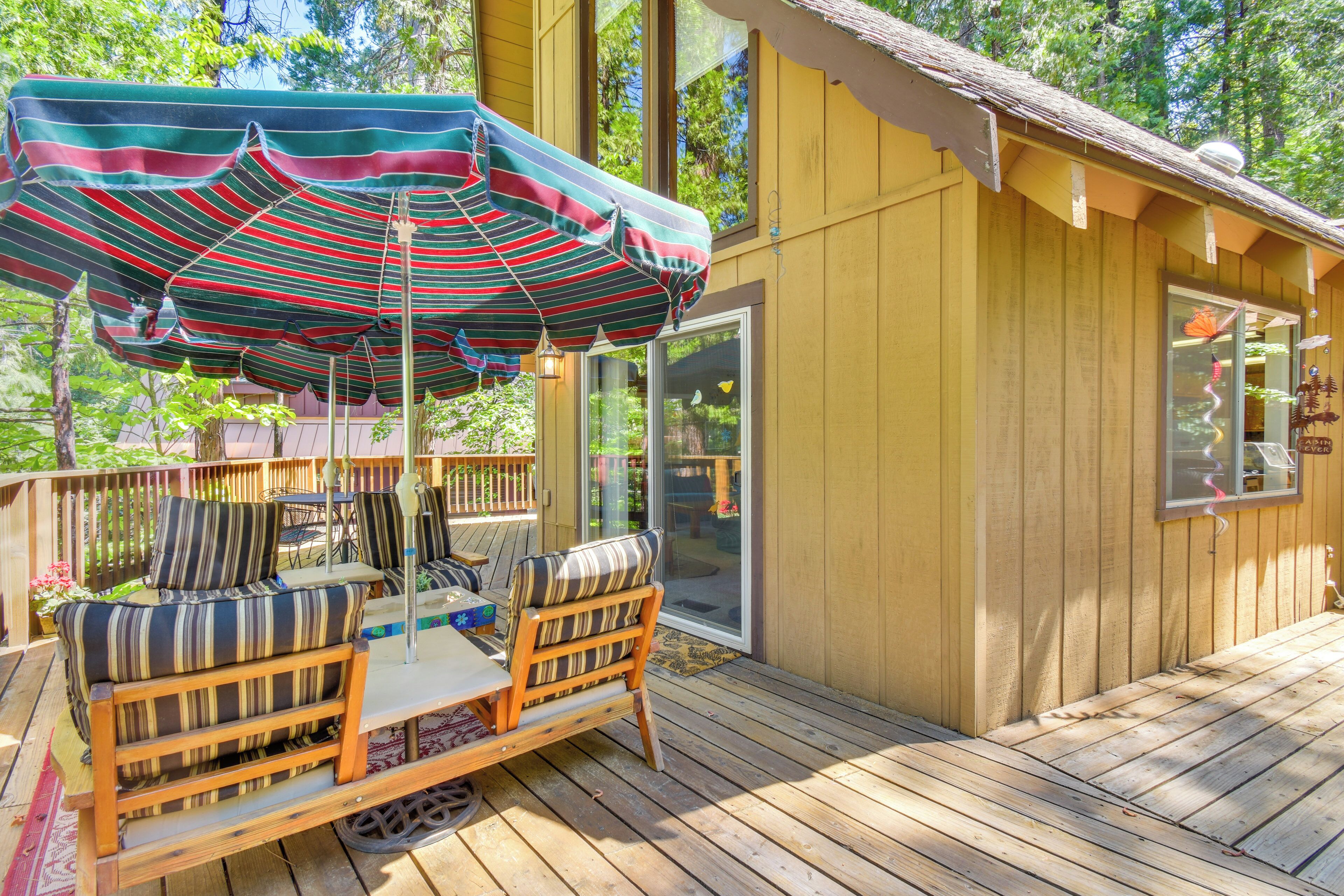 A wooden deck with a striped umbrella, outdoor furniture, and a glass door leading to a covered area.