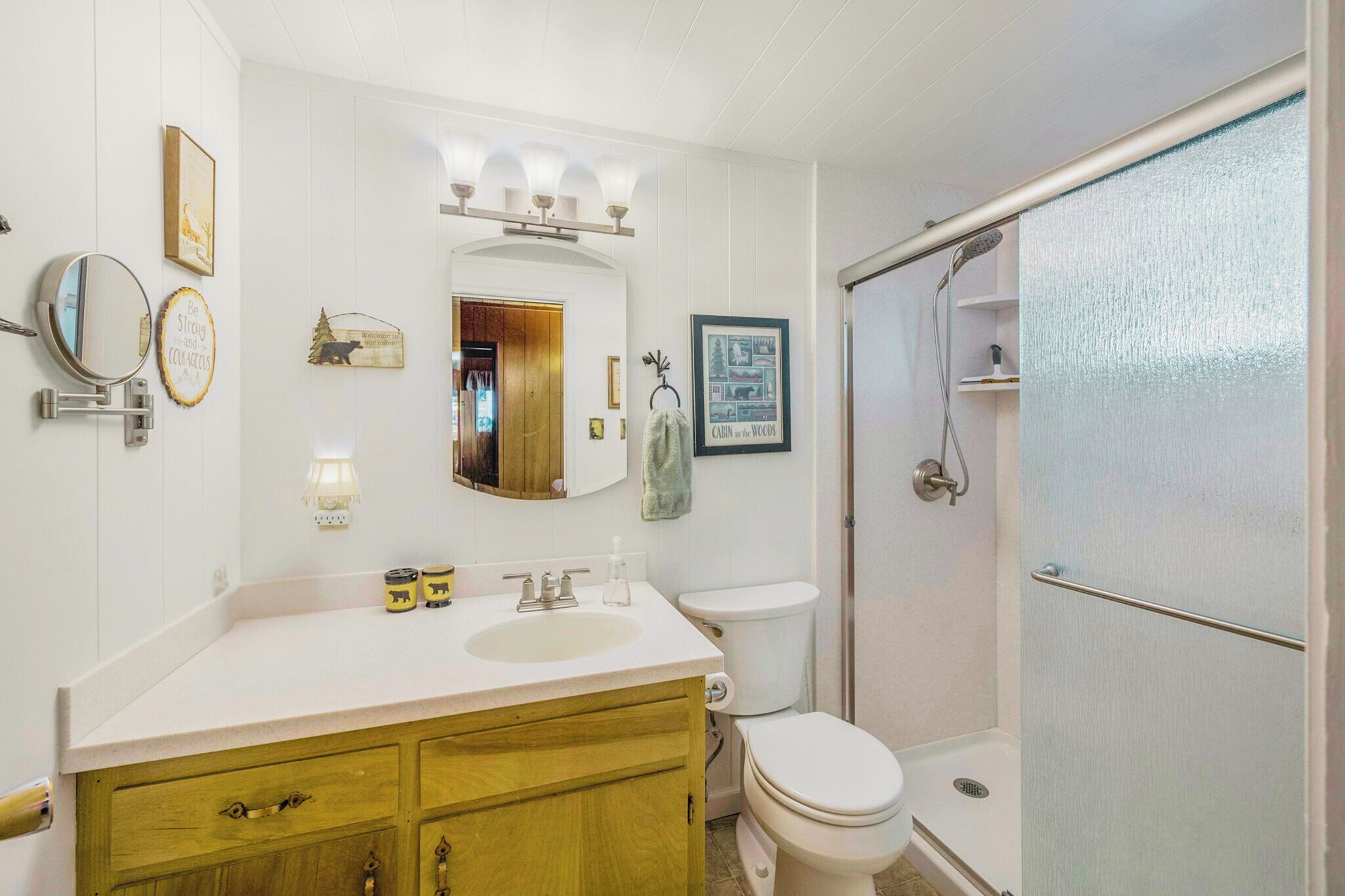 Un bagno con un mobile lavabo bianco, uno specchio rotondo, un lavandino, un WC e una cabina doccia.