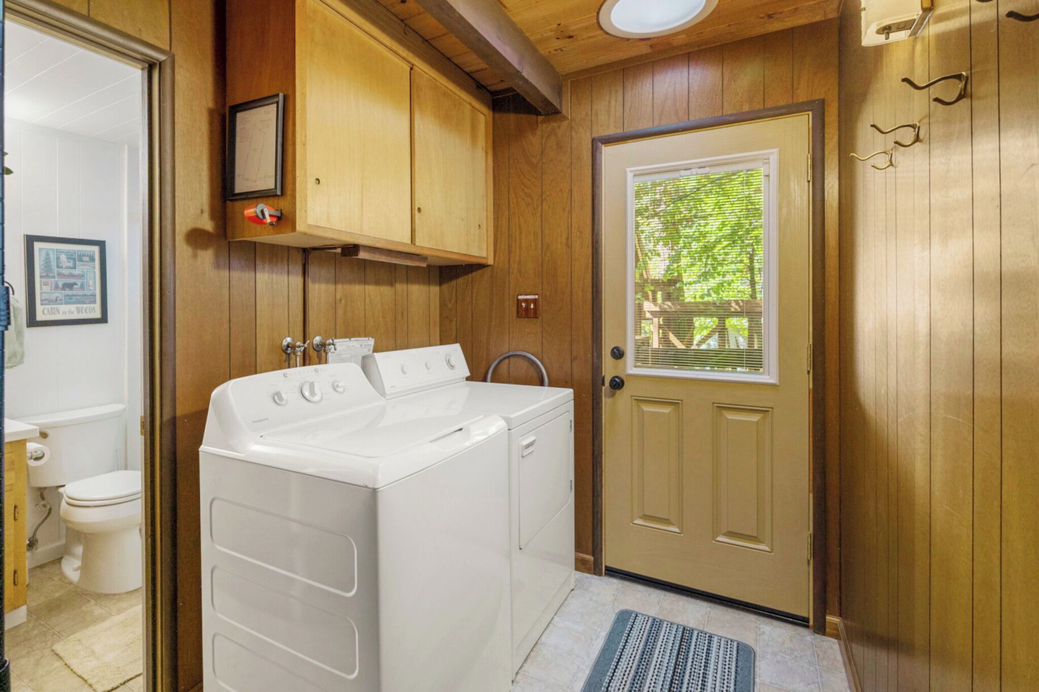 A laundry room with a washer and dryer, wooden cabinets, a door with a window, and a small framed picture on the wall.