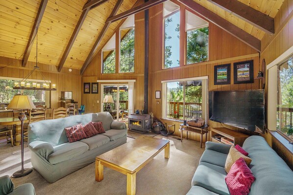 A spacious living room with high ceilings, wooden walls, and large windows. - Walk to Fly-in Lake: Blue Lake Springs Cabin! (Arnold)