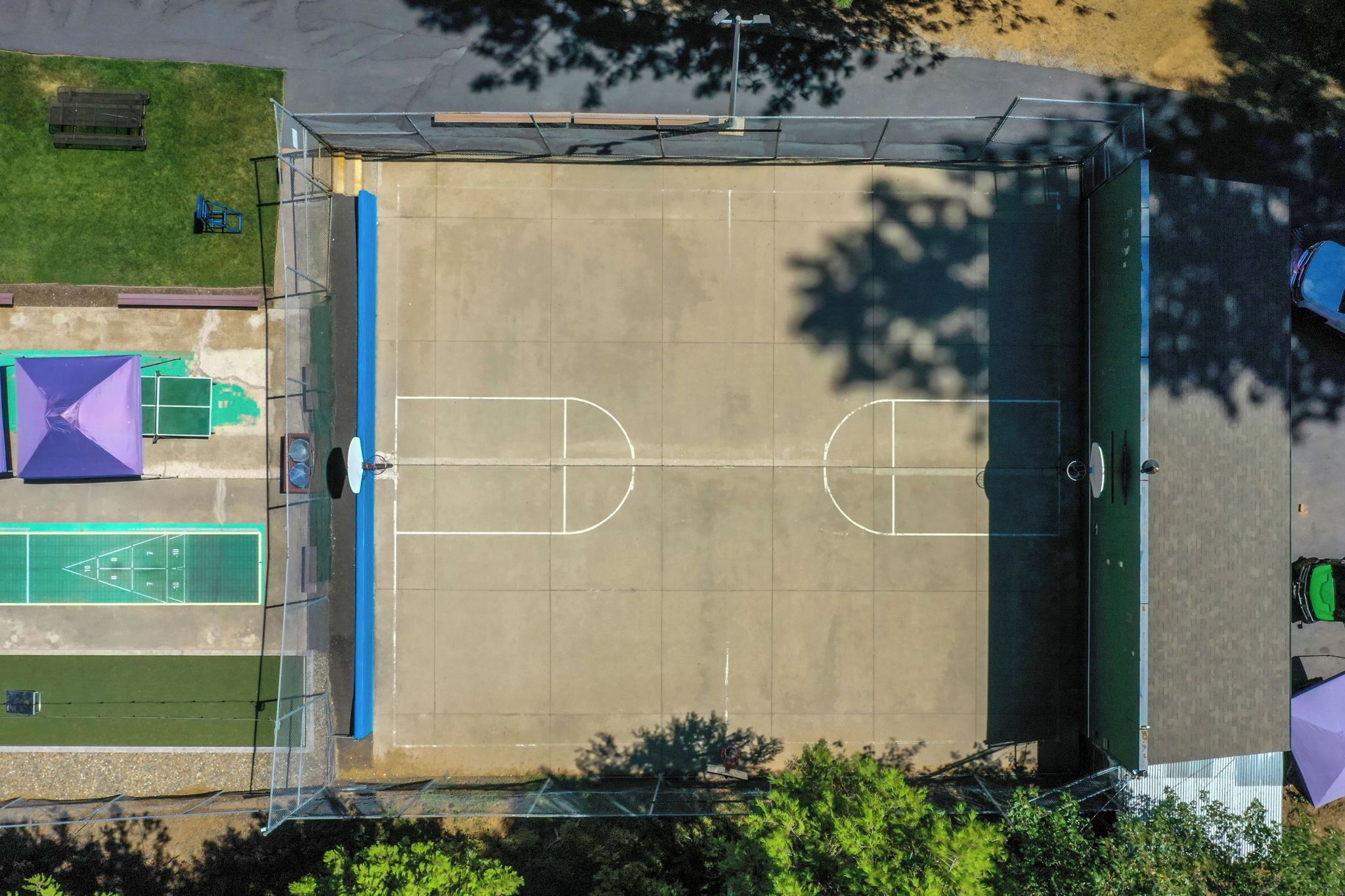 An aerial view of a sports court with a basketball court, tennis court, and a green area.