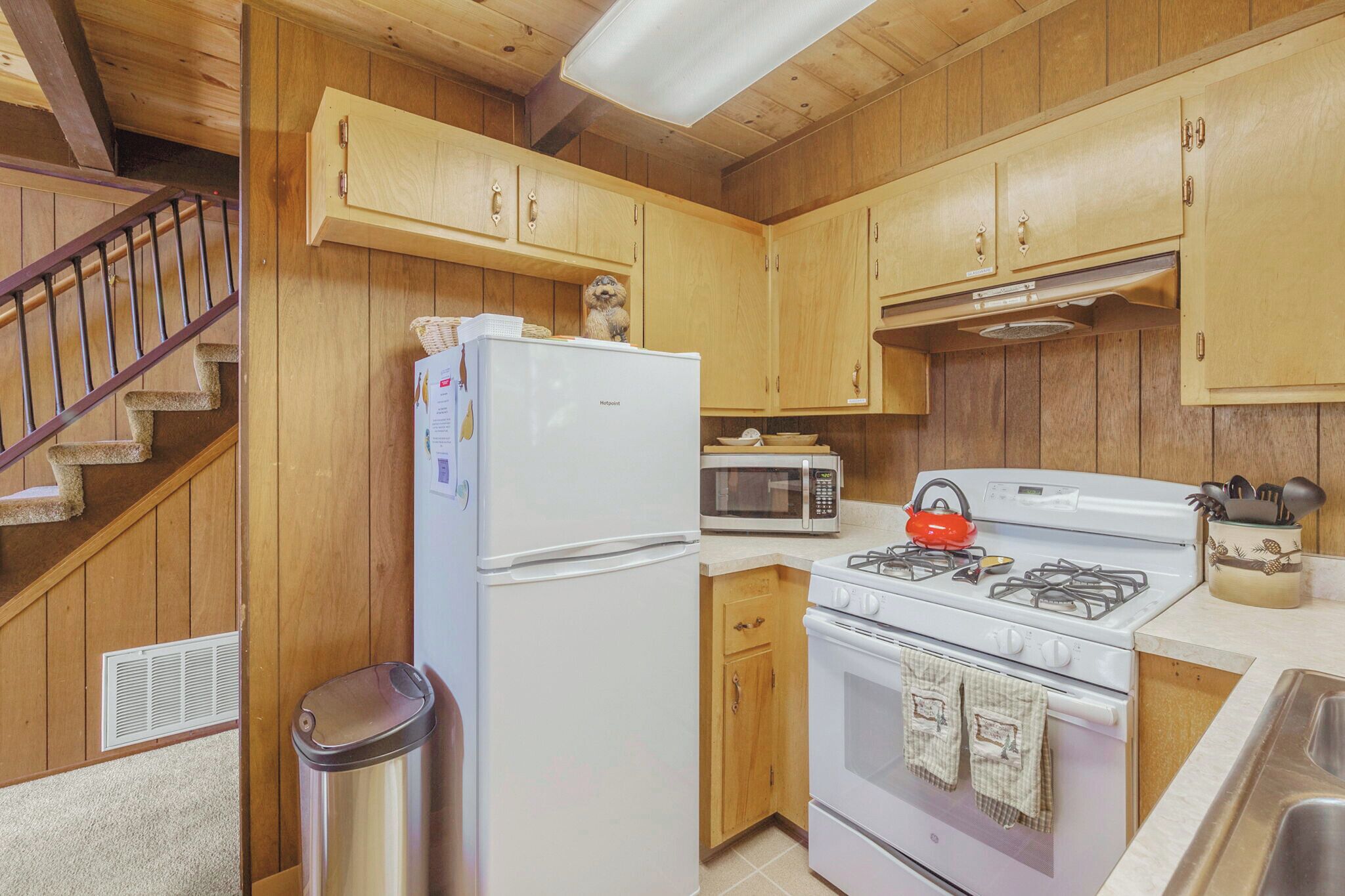 A kitchen with wooden cabinets, a white refrigerator, a microwave, a gas stove, and a trash can.