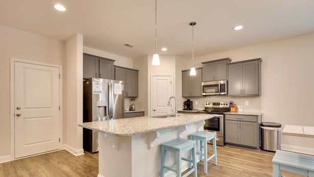 A modern kitchen with grey cabinets, stainless steel appliances, a granite countertop, and light blue bar stools. - 3 Mi to Sand & Surf: Ocean Isle Beach Retreat! (Ocean Isle Beach)