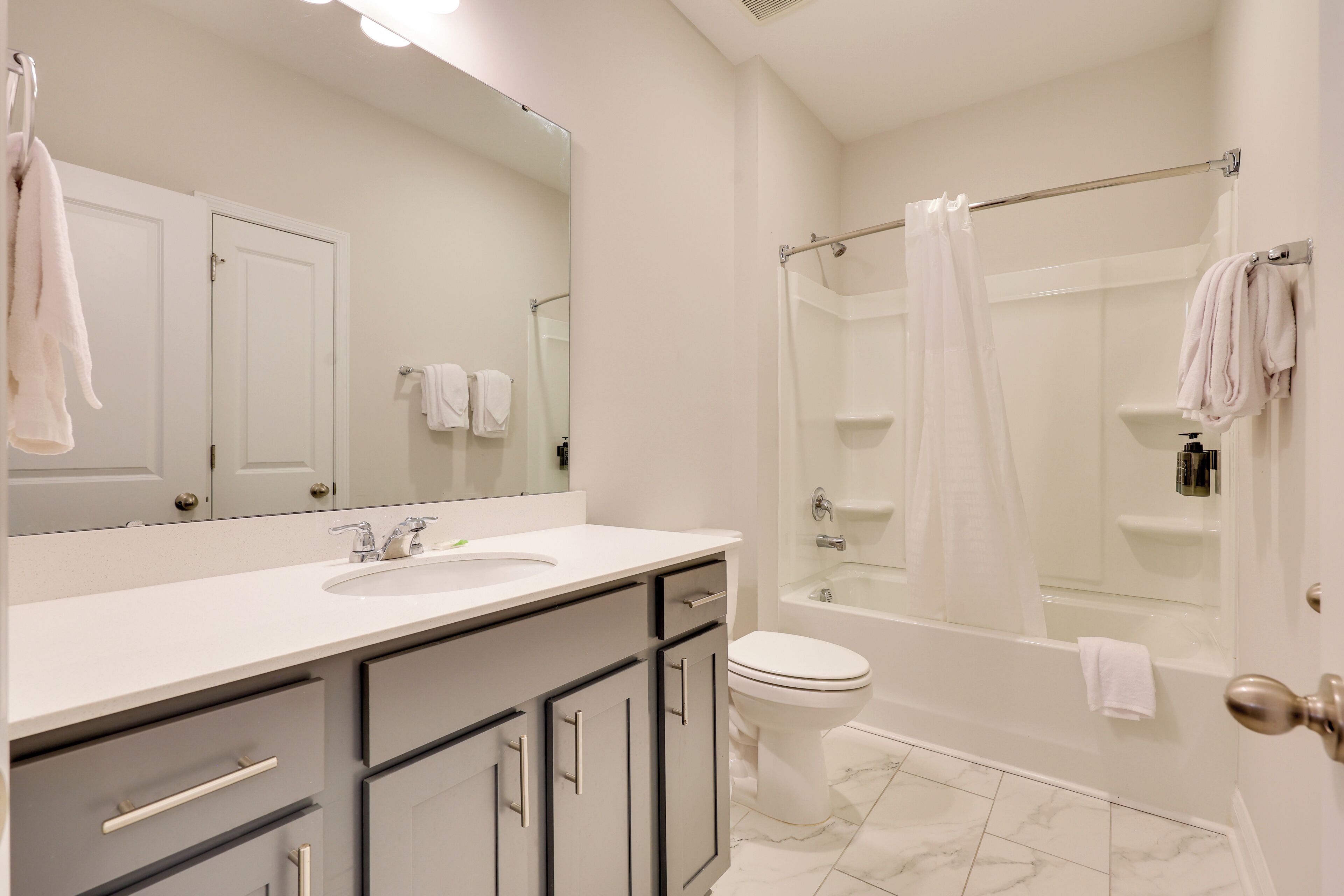 A modern bathroom with a white sink, vanity, and toilet. It includes a glass-enclosed shower and a bathtub with a shower curtain.