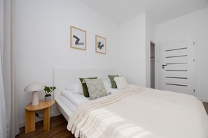 Un dormitorio con cama, mesita de noche, lámpara y dos cuadros enmarcados en la pared.