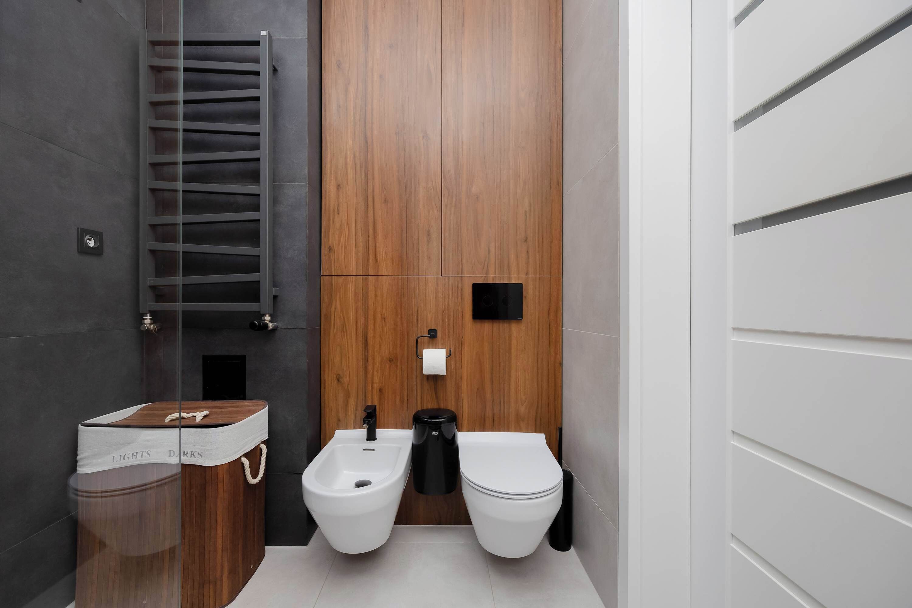 A modern bathroom with a bidet, toilet, and a wooden vanity with a trash bin.