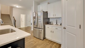 Eine moderne Küche mit weißen Schränken, einem Edelstahl-Kühlschrank, einer Mikrowelle und einer Holztreppe.