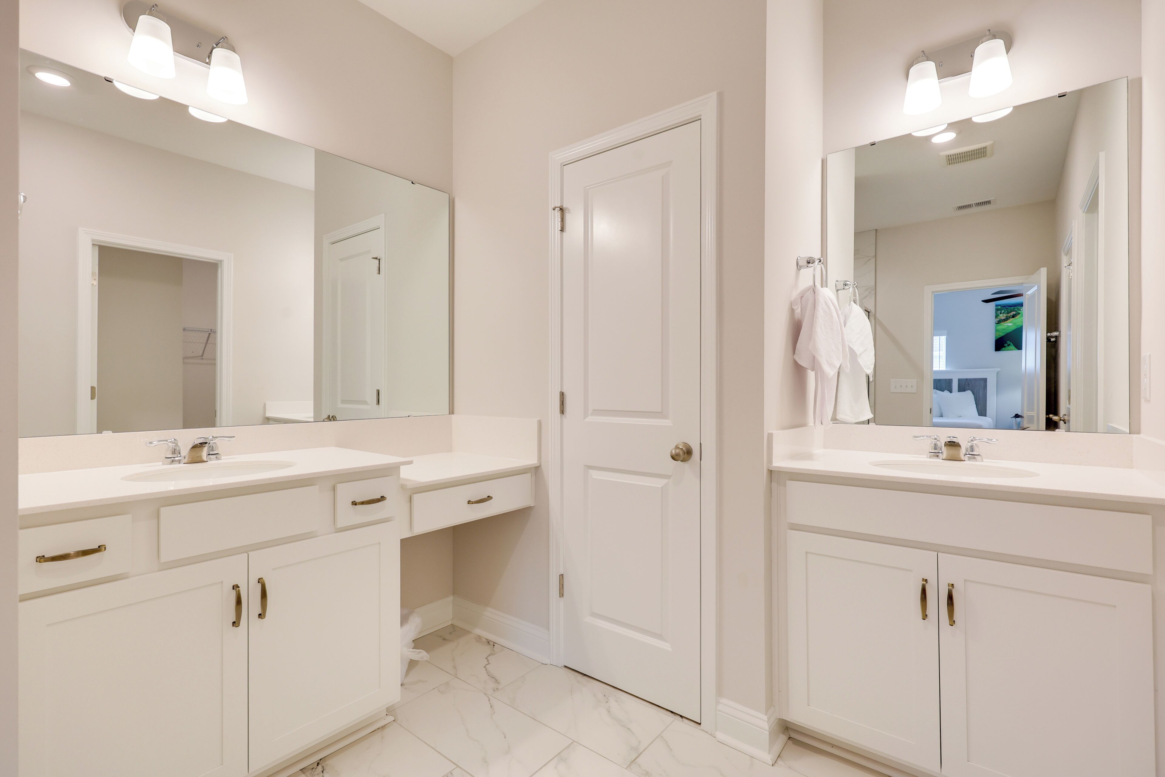 Un baño con dos lavamanos, un espejo grande y una puerta que da a otra habitación.