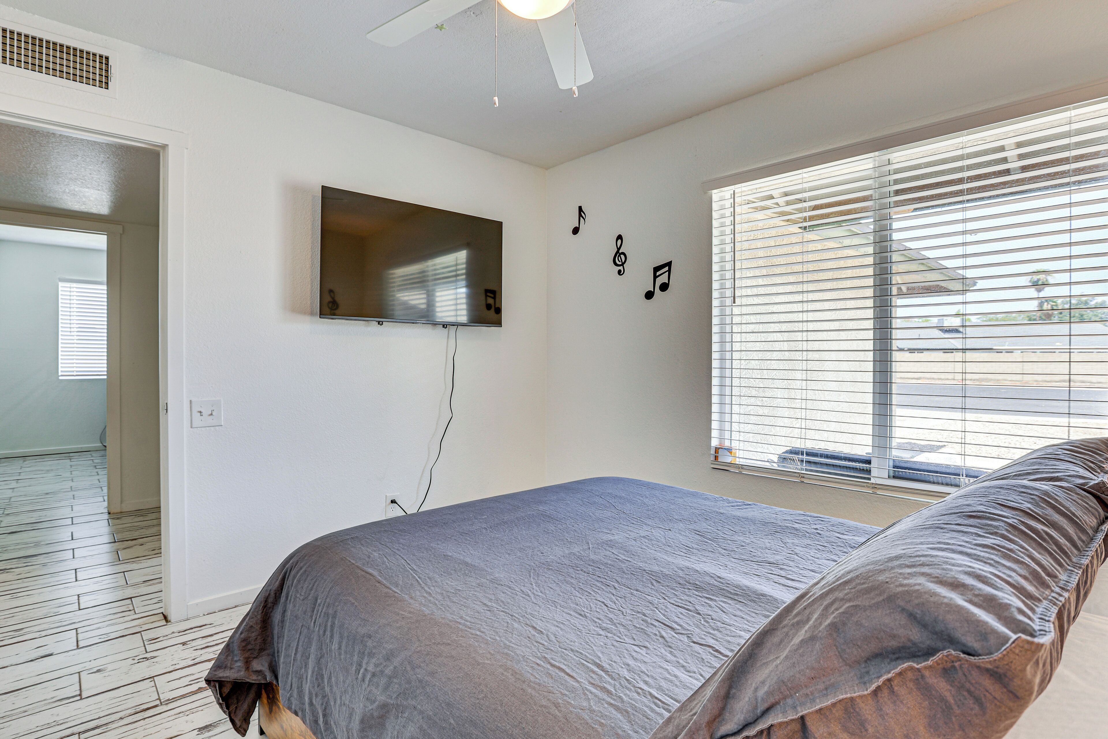 Un dormitorio con cama, televisor montado en la pared y ventana con persianas.