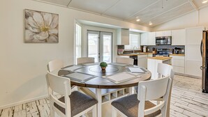 A modern kitchen with white cabinets, a stainless steel refrigerator, and a dining area with a round table and chairs. - Welcoming Group Getaway w/ Pool & Patio in Peoria! (Peoria)