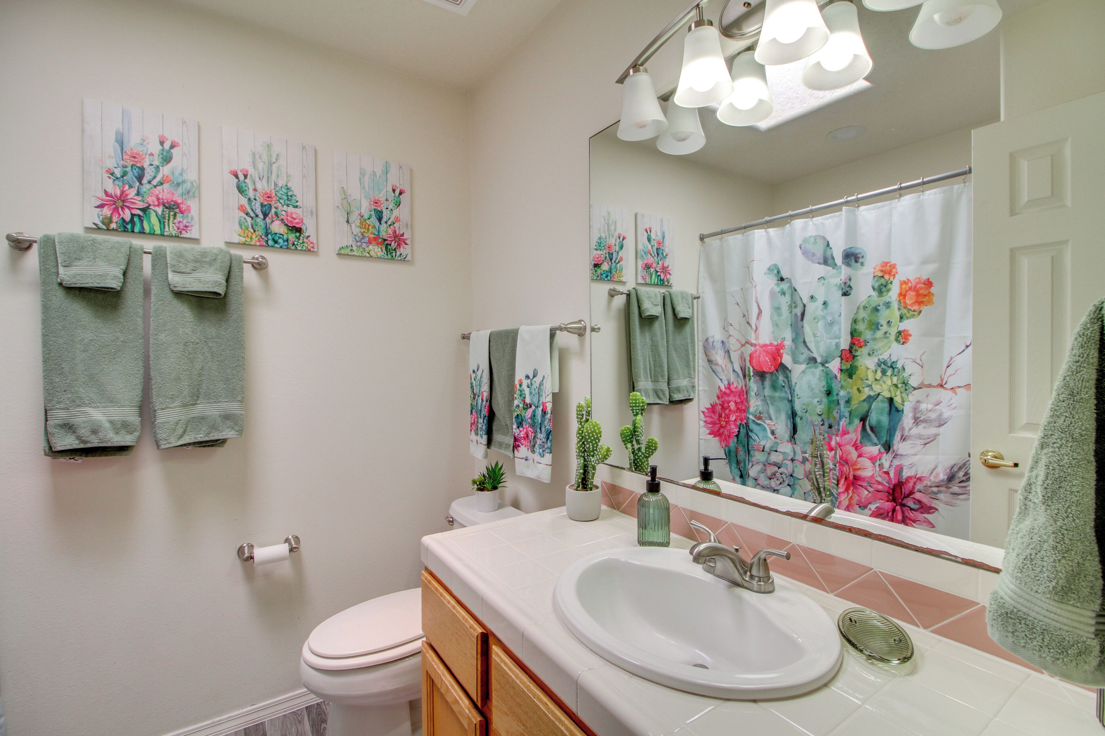 Une salle de bain avec un lavabo blanc, des toilettes et un rideau de douche orné de motifs floraux. Des serviettes sont suspendues sur un porte-serviettes et un miroir est placé au-dessus du lavabo.