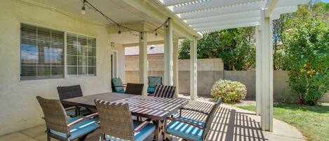 An outdoor patio with a wooden table and chairs, a pergola overhead, and a view of the backyard.