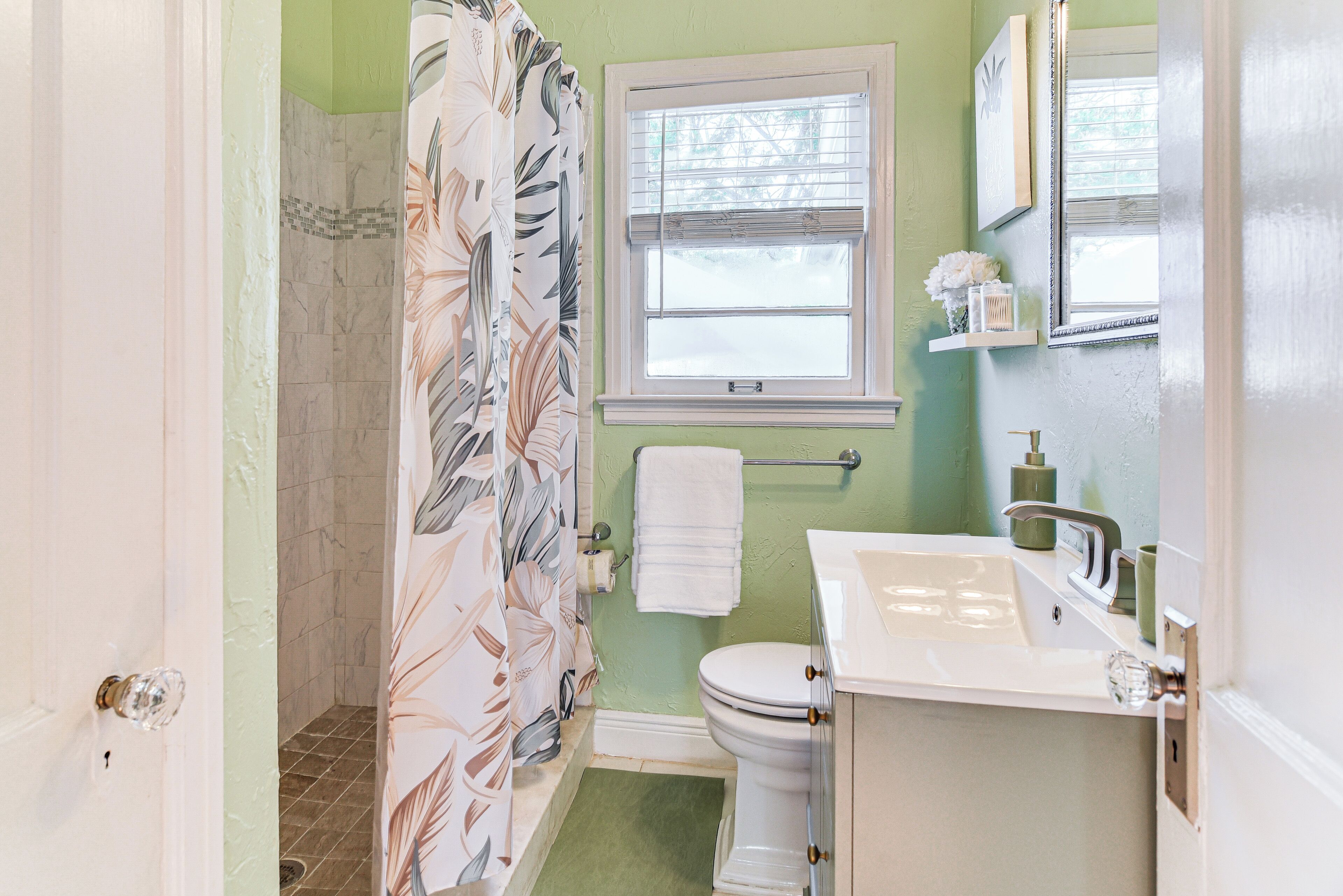 A bathroom with a shower, toilet, sink, and window.