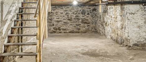 A basement with a wooden staircase leading up, a stone wall, and visible plumbing.
