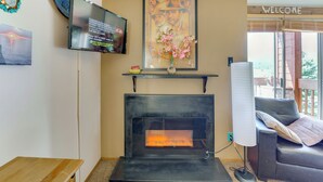 A living room with a fireplace, a television mounted on the wall, and a 'WELCOME' sign above a window. - Walk to Angel Fire Resort: Getaway w/ Balcony (Angel Fire)