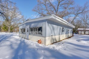 Ein kleines, eingeschossiges Gebäude mit flachem Dach und großen Fenstern, umgeben von Schnee und kahl stehenden Bäumen.