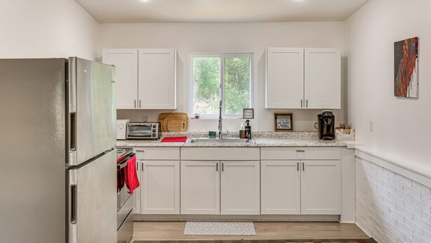 A modern kitchen with white cabinets, a stainless steel refrigerator, a toaster, and a window providing natural light. - Pet-friendly Retreat: Over 3 Acres in Baldwin! (Baldwin)