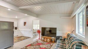 A modern living room with a large flat-screen TV, a sofa, and a dining area with a red fan. - Pet-friendly Retreat: Over 3 Acres in Baldwin! (Baldwin)