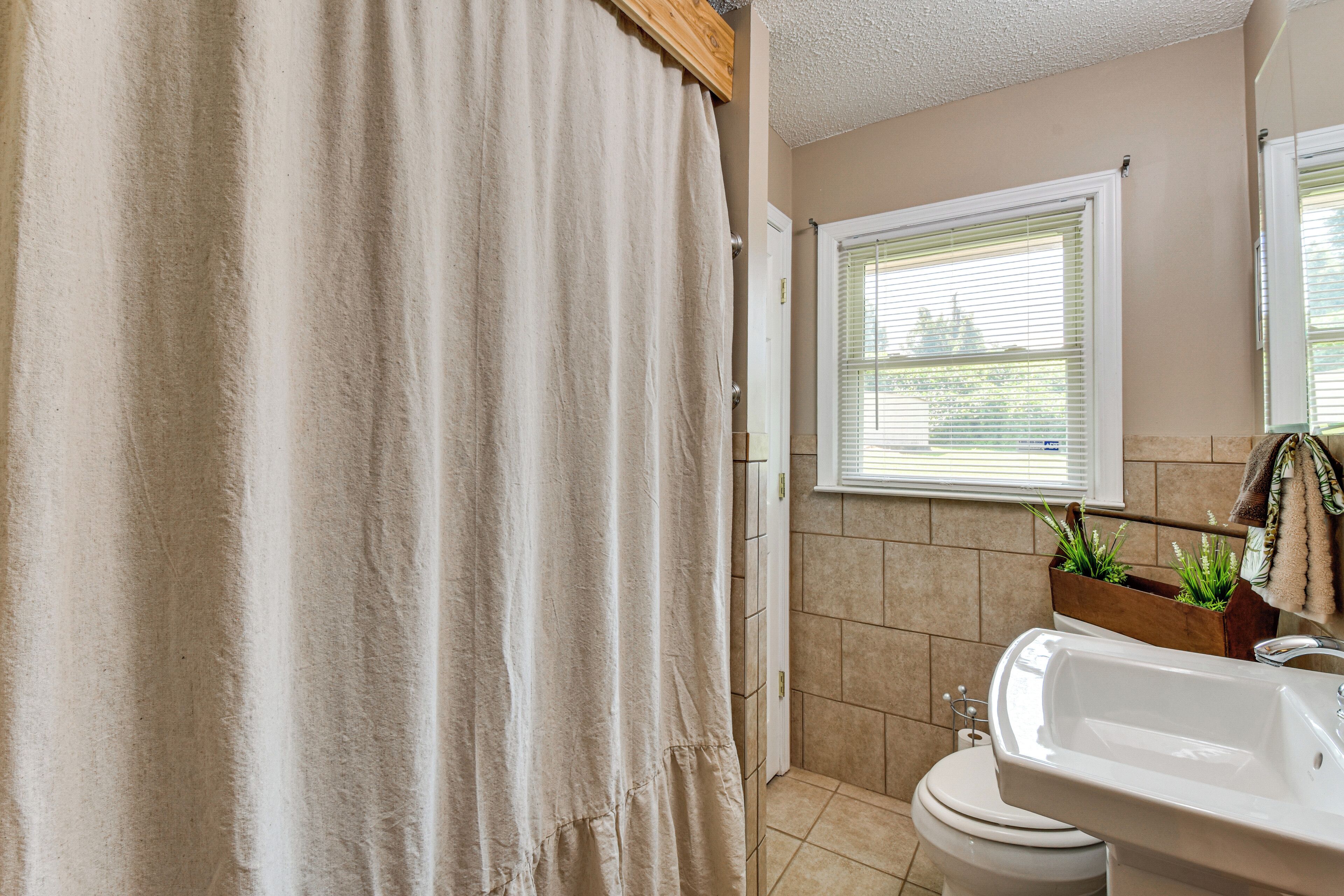 A bathroom with a shower curtain, toilet, sink, and window with blinds.