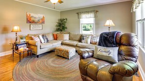 A living room with a sofa, ottoman, and a leather chair with a 'Family' pillow. There is a ceiling fan, a plant, and a window with curtains. - 8 Mi to Clemson: Peaceful Family Home w/ Yard (Seneca)