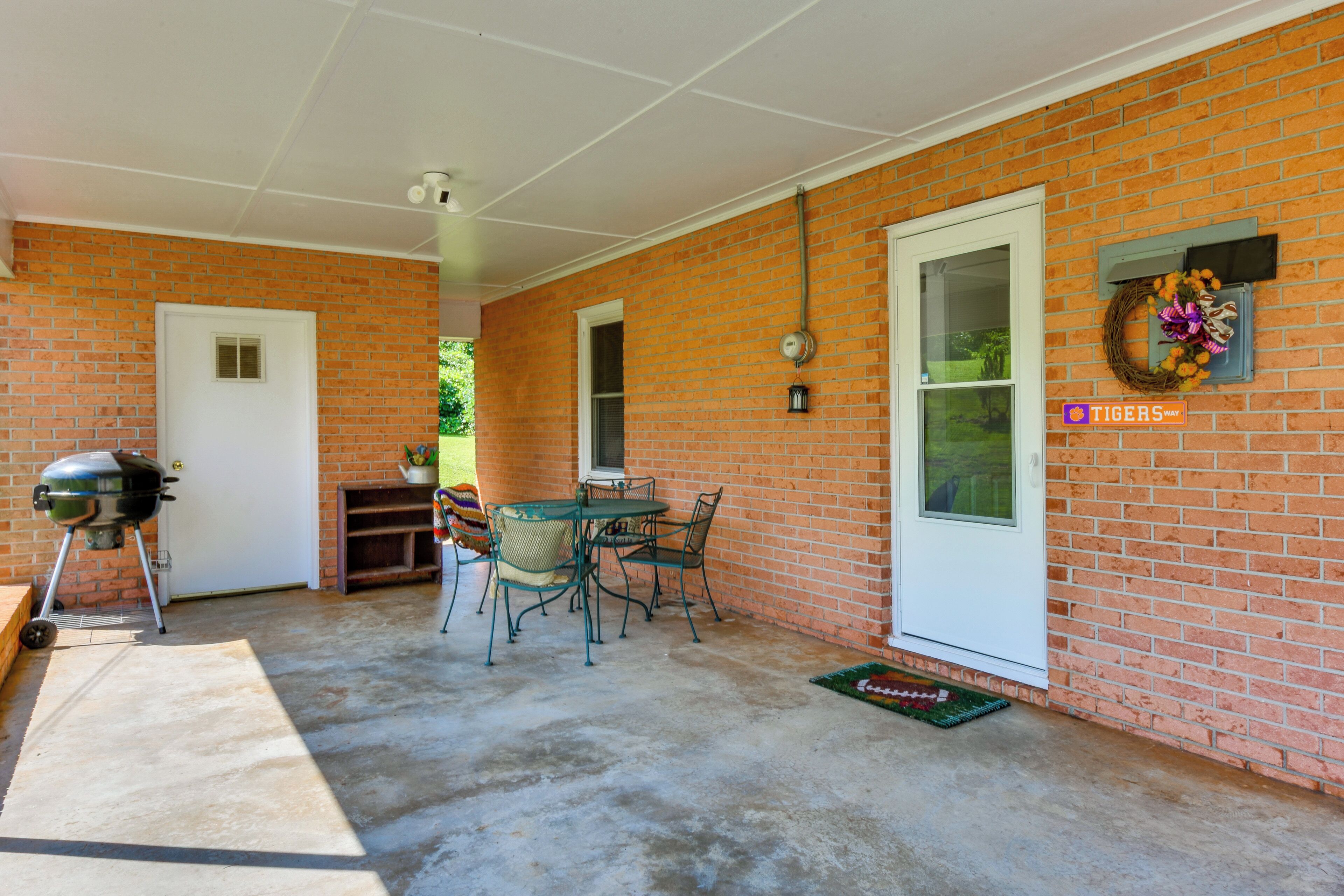 Eine überdachte Terrasse mit Backsteinmauer, Grill, Tisch und Stühlen sowie einer Tür.