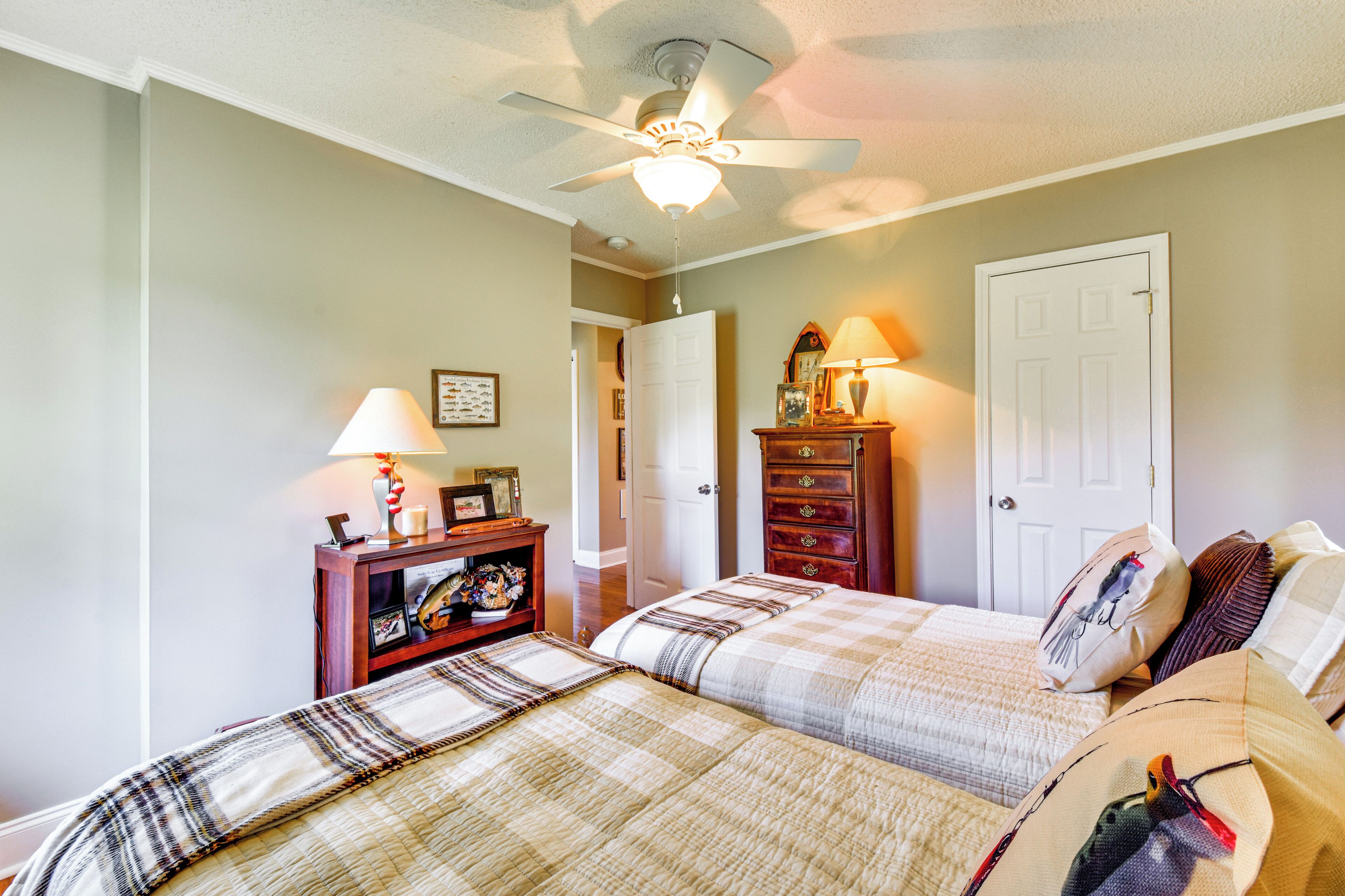A bedroom with two beds, a ceiling fan, a dresser, and a nightstand with a lamp.