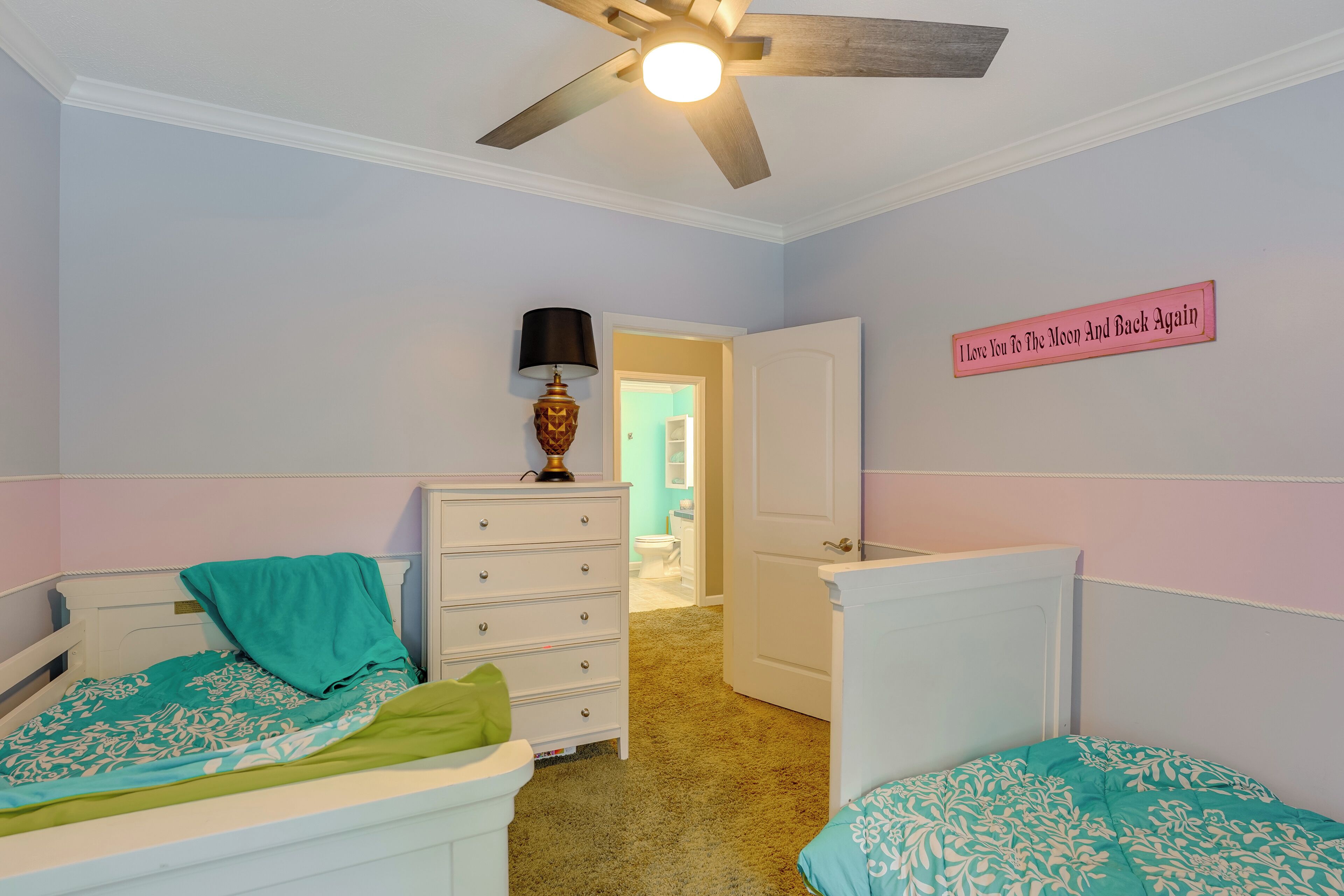 Une chambre avec deux lits, une commode, une lampe et un ventilateur de plafond.