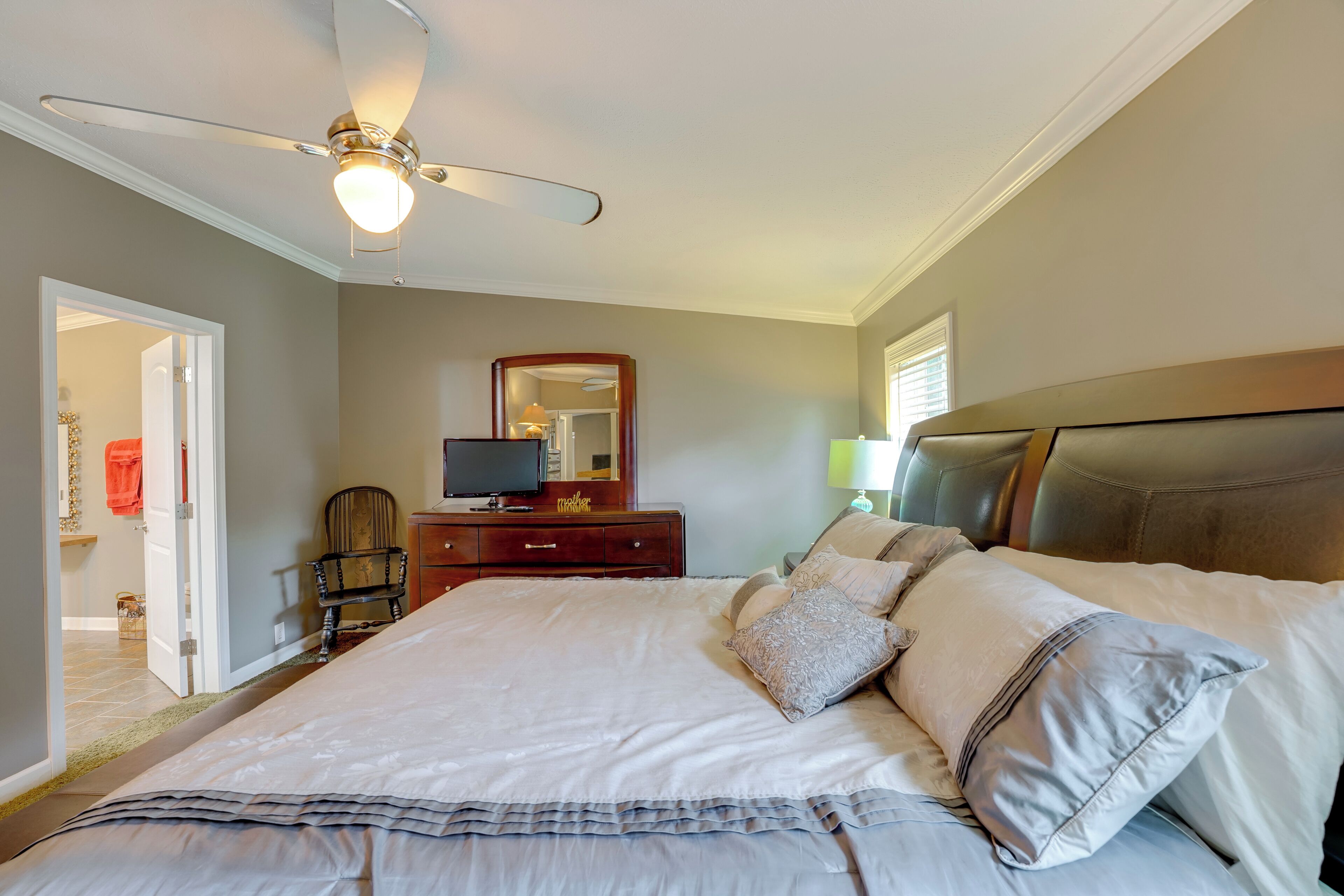 Une chambre à coucher avec un grand lit, un ventilateur de plafond, une commode, une chaise et un miroir.