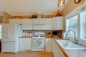 A kitchen with white cabinets, a stove, a refrigerator, a microwave, and a sink. - Fall Hikes & ORV Trails: Cozy Mears Retreat (Mears)