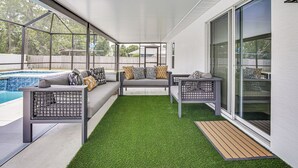 Un patio cubierto con piscina, un sofá gris y una mesita con cojines.