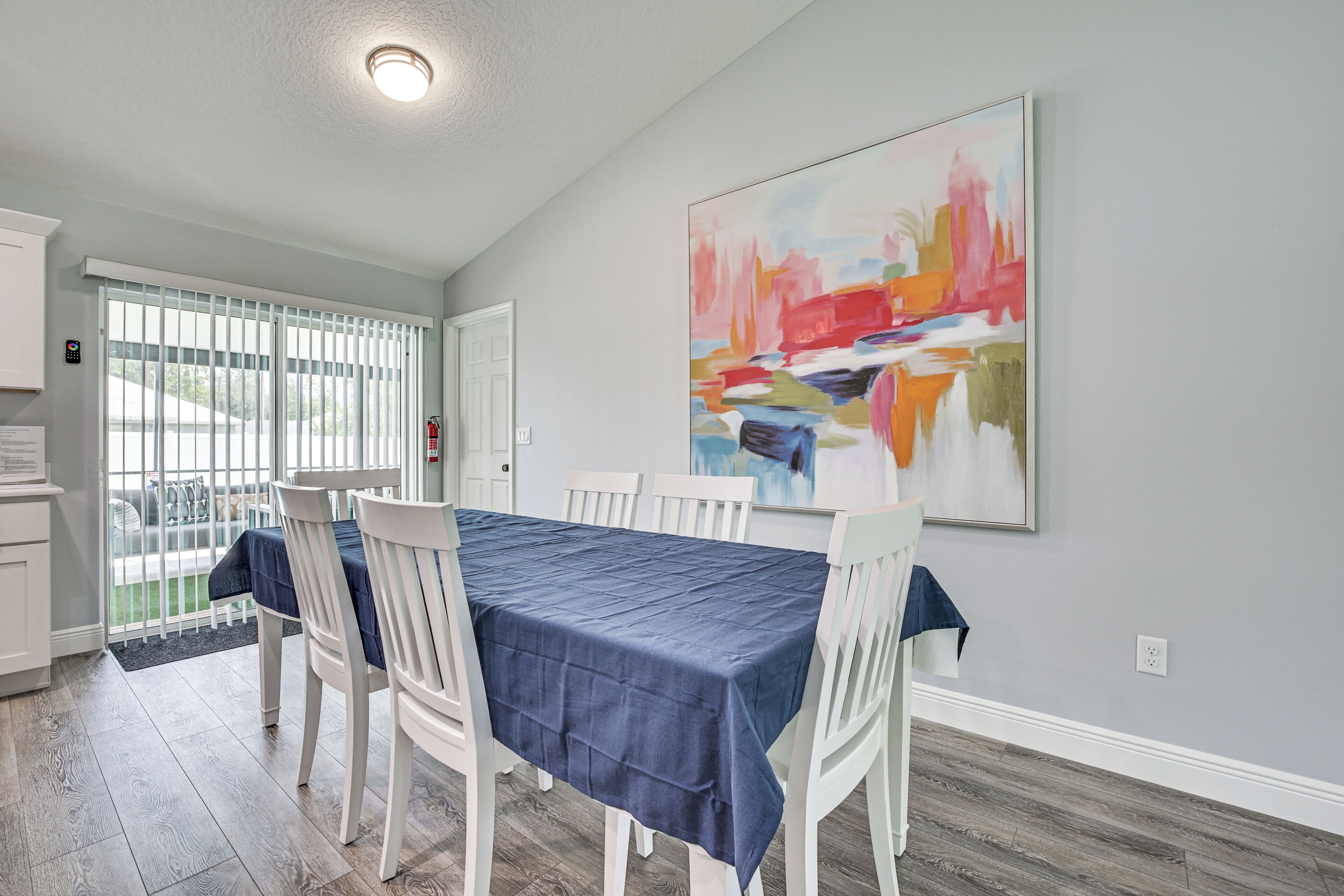 Comedor con una mesa dispuesta para cuatro, sillas blancas y un mantel azul.