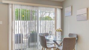 A dining area with a glass table and four chairs, a vase with flowers, and a sliding glass door leading to an outdoor space. - Steps to Park: Dog-friendly Condo in Conyers! (Conyers)