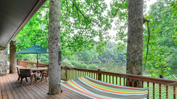 Eine Holzterrasse mit einer Hängematte, einem Tisch und Stühlen mit Blick auf ein bewaldetes Gebiet.