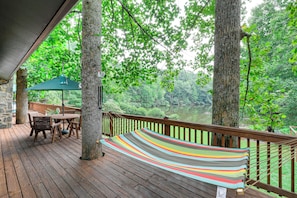 A wooden deck with a hammock, a table, and chairs, overlooking a forested area. - Deck & Game Room! Lakefront Blue Ridge Mtn Gem (Deep Gap)