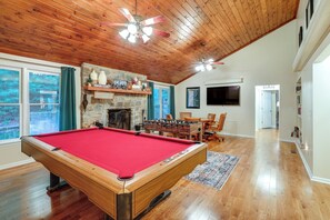 A pool table in a room with wooden floors, a stone fireplace, and a ceiling fan. - Deck & Game Room! Lakefront Blue Ridge Mtn Gem (Deep Gap)
