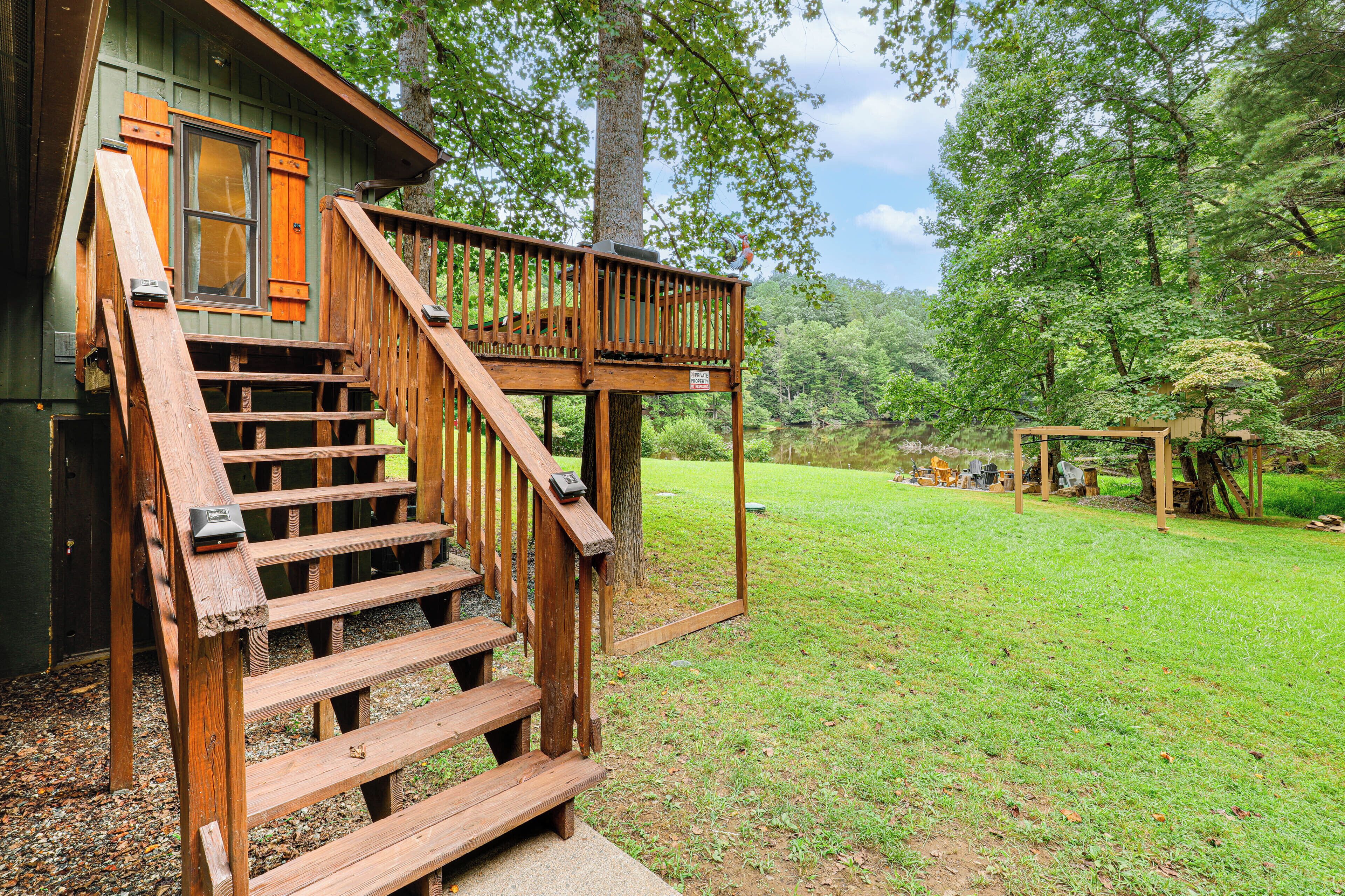 A wooden staircase leading to a deck with a view of a grassy area and trees.